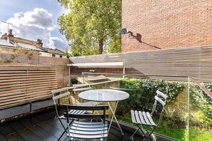 Eine Terrasse mit einem runden Tisch, Stühlen, einer Ziegelmauer und einem Baum.