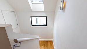 Un escalier avec des marches en bois menant à un palier, une lucarne et un luminaire fixé au mur.