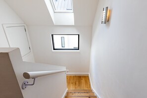 Eine Treppe mit Holzbodenstufen führt zu einer Zwischenebene, einem Oberlicht und einer Wandleuchte.