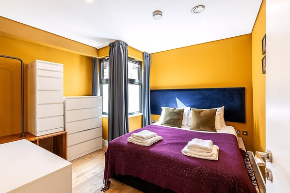 Ein Hotelzimmer mit einem Bett, einem Schrank, einem Schreibtisch und einem Fenster mit Vorhängen.