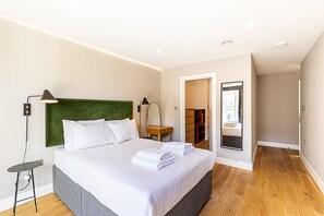 Quarto moderno com uma cama grande, mesas de cabeceira, espelho e um closet espaçoso.
