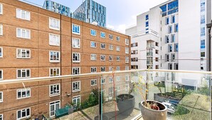 Un immeuble de grande hauteur doté de nombreuses fenêtres et de balcons, d’une rambarde en verre et de plantes en pot sur le balcon.