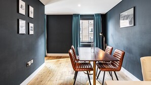 Une salle à manger moderne avec un mur foncé, une table en bois, des chaises en cuir et une fenêtre avec des rideaux.