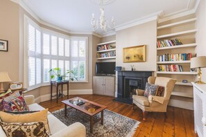 Ein Wohnzimmer mit Kamin, Bücherregalen, einem Fernseher und einem Erkerfenster.