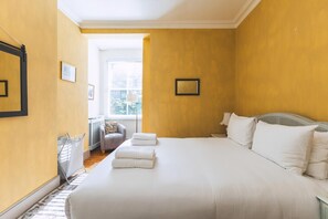 A hotel room with a large bed, a sitting area with a chair and a table, and a window with a view. - Charming Ground Floor Flat, West Kensington (London)