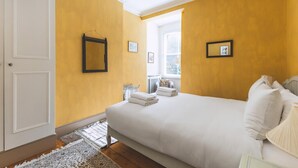 Een slaapkamer met een bed, een raam, een deur en een kroonluchter.