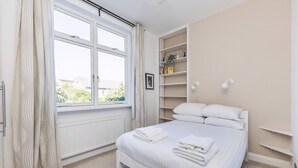 Ein Schlafzimmer mit Bett, Fenster, Heizkörper, Regalen und einem Bild.