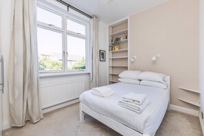 A bedroom with a bed, window, radiator, shelves, and a picture. - Stylish West London Stay by Hammersmith (London)
