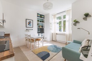 A modern living room with a sofa, a dining table with chairs, a TV, and a bookshelf. - Stylish West London Stay by Hammersmith (London)