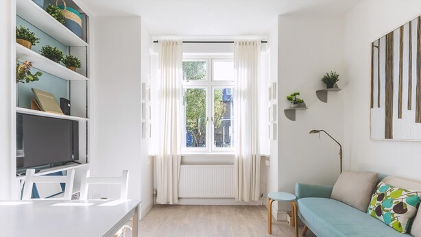 Ein modernes Wohnzimmer mit einer Couch, einem kleinen Tisch, einem Fernseher und Regalen mit Pflanzen.