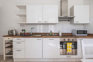 A modern kitchen with white cabinets, a wooden countertop, a stainless steel oven, and a microwave. - Stylish West London Stay by Hammersmith (London)