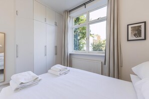 A hotel room with a bed, a window with curtains, a radiator, and a framed picture on the wall. - Stylish West London Stay by Hammersmith (London)
