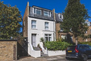 A two-story residential building with a white facade, a dark roof, and a visible garage door. - Stylish West London Stay by Hammersmith (London)