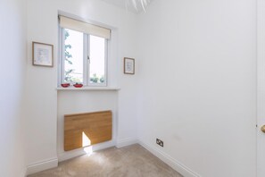 A room with a window, a radiator, and two framed pictures on the wall. - Stylish West London Stay by Hammersmith (London)
