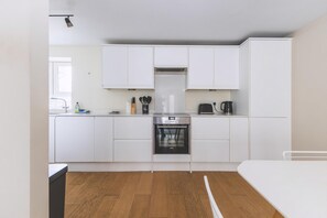 A modern kitchen with white cabinets, a built-in oven, and a coffee maker. - 2BR Central Belgravia Retreat (London)