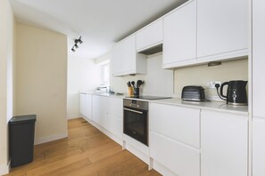 Eine moderne Küche mit weißen Schränken, einem eingebauten Backofen, einer Kaffeemaschine und einem Mülleimer.