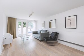 Ein modernes Wohnzimmer mit einer Couch, einem Glastisch, einem schwarzen Sessel und gerahmten Kunstwerken an den Wänden.
