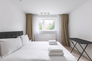 Ein Hotelzimmer mit Bett, Fenster mit Vorhängen, Nachttisch und Heizkörper.
