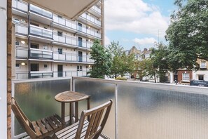 Uma varanda com mesa e cadeiras, com vista para uma área residencial com edifícios altos e árvores.
