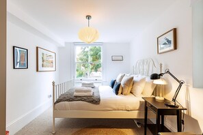 Ein Schlafzimmer mit Bett, Nachttisch, Lampe, Fenster und gerahmten Bildern an der Wand.