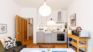 Cocina compacta con una isla central, zona de comedor con mesa y sillas, y una puerta de madera que da a otra habitación.