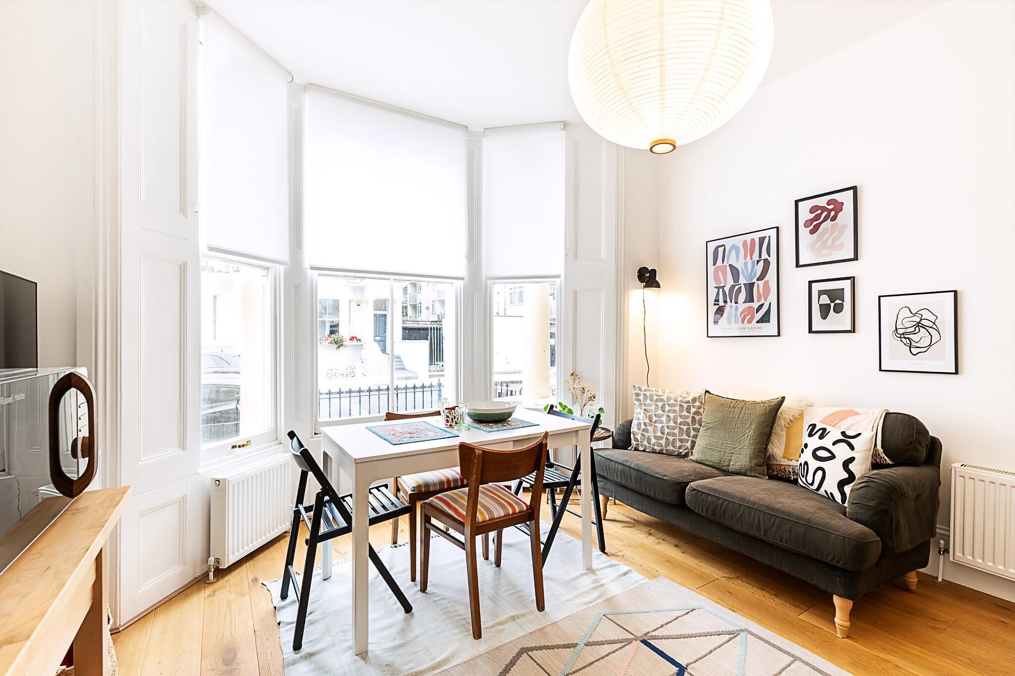 A bright living room with a dining table, sofa, and large windows.