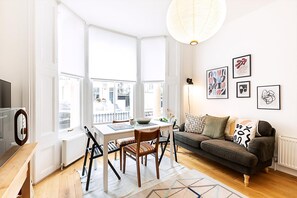 Ein helles Wohnzimmer mit Esstisch, Sofa und großen Fenstern.
