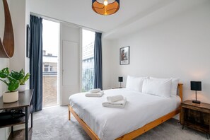 A bedroom with a bed, a desk, a chair, a potted plant, and a view of the outside. - Stylish 2-bed Apartment in Southwark (London)