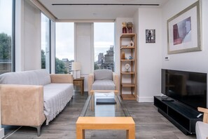 A modern living room with a sofa, armchair, coffee table, TV, and a bookshelf. - Stylish 2-bed Apartment in Southwark (London)