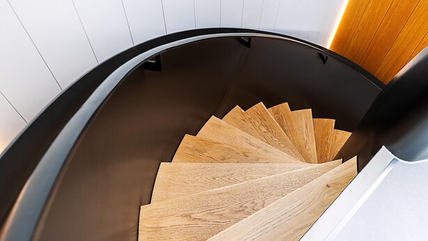 Un escalier en colimaçon moderne, avec des marches en bois et une rampe noire.