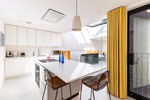 Eine moderne Küche mit weißen Schränken, einer zentralen Kochinsel und einem Essbereich mit Stühlen.