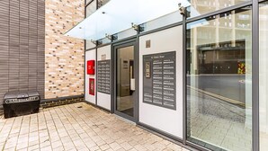 L'ingresso di un edificio con una porta in vetro, una targa con l'indicazione '12 Oiselle Road' e un cestino con la scritta 'SALT & GRIT'.