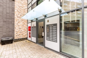 A building entrance with a glass door, a sign for '12 Oiselle Road,' and a trash bin labeled 'SALT & GRIT.' - Modern 2-bed Apartment by the Thames (London)