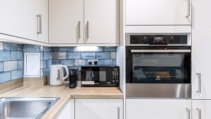 Una cucina con mobili bianchi, forno in acciaio inossidabile, microonde e macchina del caffè.