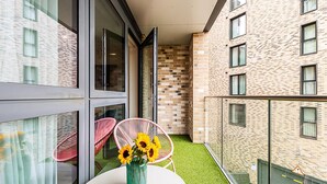 Un balcone con una porta vetrata, un muro in mattoni e un tavolino con un vaso di girasoli.
