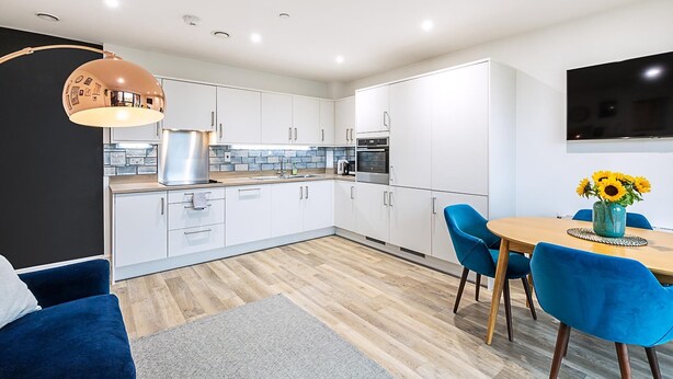 Una cucina moderna con mobili bianchi, un piano di lavoro in legno e una zona pranzo con sedie blu e un tavolo.