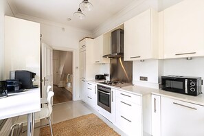 A modern kitchen with white cabinetry, stainless steel appliances, and a dining area with a white table and chairs. - Bright 3-bedroom Family Home Near Little Venice (London)