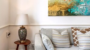 Ein Wohnzimmer mit einer Couch, Zierkissen, einer Lampe und einem farbenfrohen abstrakten Gemälde an der Wand.