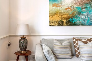A living room with a sofa, decorative pillows, a lamp, and a colorful abstract painting on the wall. - Bright 3-bedroom Family Home Near Little Venice (London)