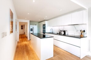 A modern kitchen with white cabinetry, a central island, and a wooden floor. - Riverside Luxury With Iconic Views (London)