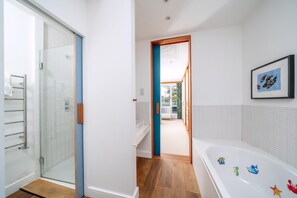 A modern bathroom with a glass shower, a bathtub with colorful animal decals, and a framed picture on the wall. - Stylish Family Retreat in Trendy Hackney (London)