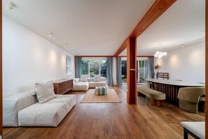 A modern living room with a wooden floor, a sofa set, a bench, and a dining area with a table and chairs. - Stylish Family Retreat in Trendy Hackney (London)
