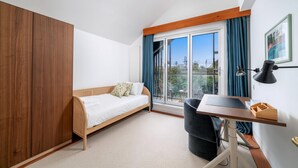 A bedroom with a bed, desk, chair, wardrobe, and large window with curtains. - Stylish Family Retreat in Trendy Hackney (London)