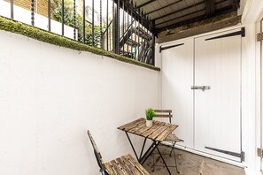 A small outdoor patio area with a wooden table and bench, a potted plant, and a white door. - Chelsea Riverside Modern Escape (London)