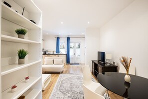 A modern living room with a sofa, a dining table, and a TV. There is a kitchen area with a sink and cabinets. - Chelsea Riverside Modern Escape (London)
