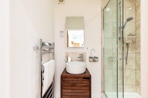 A modern bathroom with a glass shower enclosure, a wooden vanity, a white sink, and a mirror above the sink. - Chelsea Riverside Modern Escape (London)