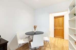 A room with a round table, white chairs, a wooden door, and a white shelving unit. - Chelsea Riverside Modern Escape (London)