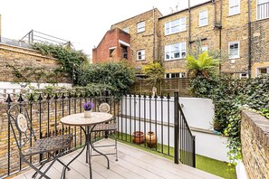 A patio with a table and chairs, surrounded by a fence and greenery. - Elegant Chelsea Riverside Garden Retreat (London)