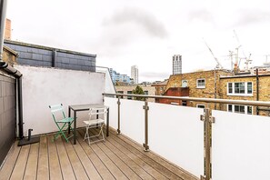 Eine Dachterrasse mit Tisch und Stühlen, einem weißen Geländer und Blick auf Stadtgebäude.