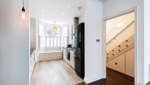 A modern kitchen with a black refrigerator, white cabinetry, and a wooden floor. - Elegant Chelsea Riverside Garden Retreat (London)